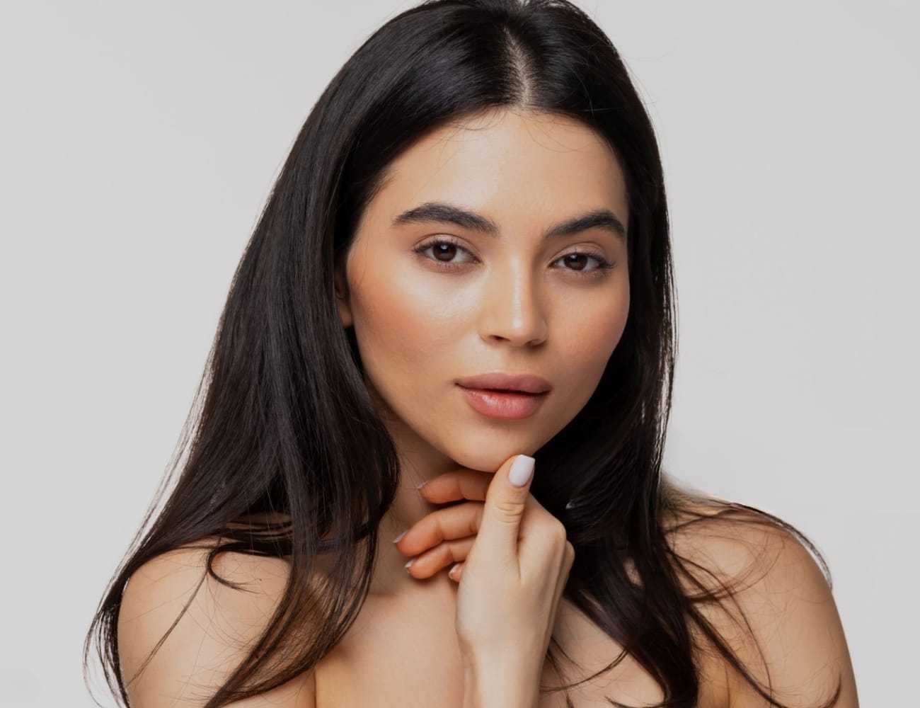 Portrait of a woman with long dark hair, softly smiling and resting her chin on her hand.