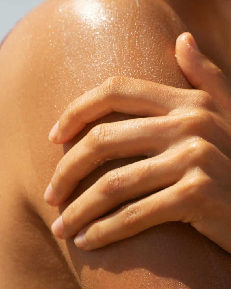 Close-up of a hand resting on a sunlit shoulder with glistening skin.