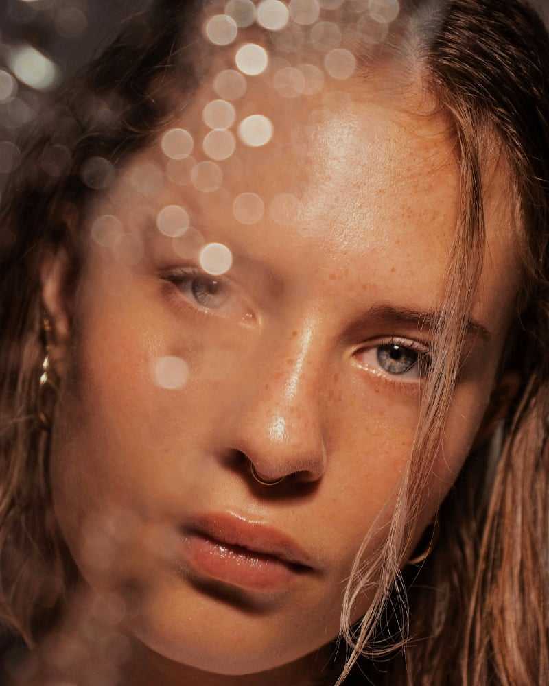 Young woman with wet hair and a thoughtful expression through a blurry glass effect.